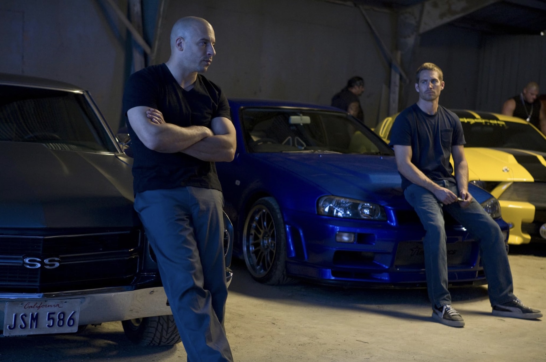 Vin Diesel y Paul Walker se paran frente a sus autos en Fast & Furious 4.