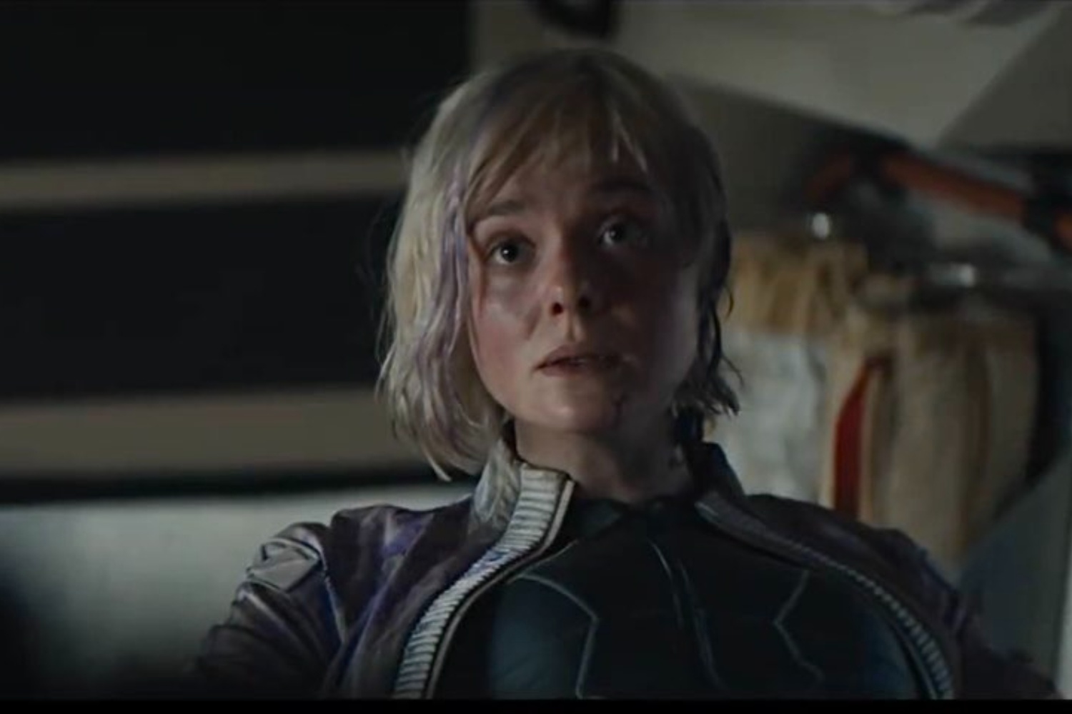 Elle Fanning sits down and looks at something.
